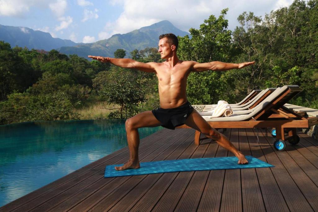 贝里胡罗亚Sennya Resorts的做瑜伽的男人在泳池旁的瑜伽垫上摆姿势
