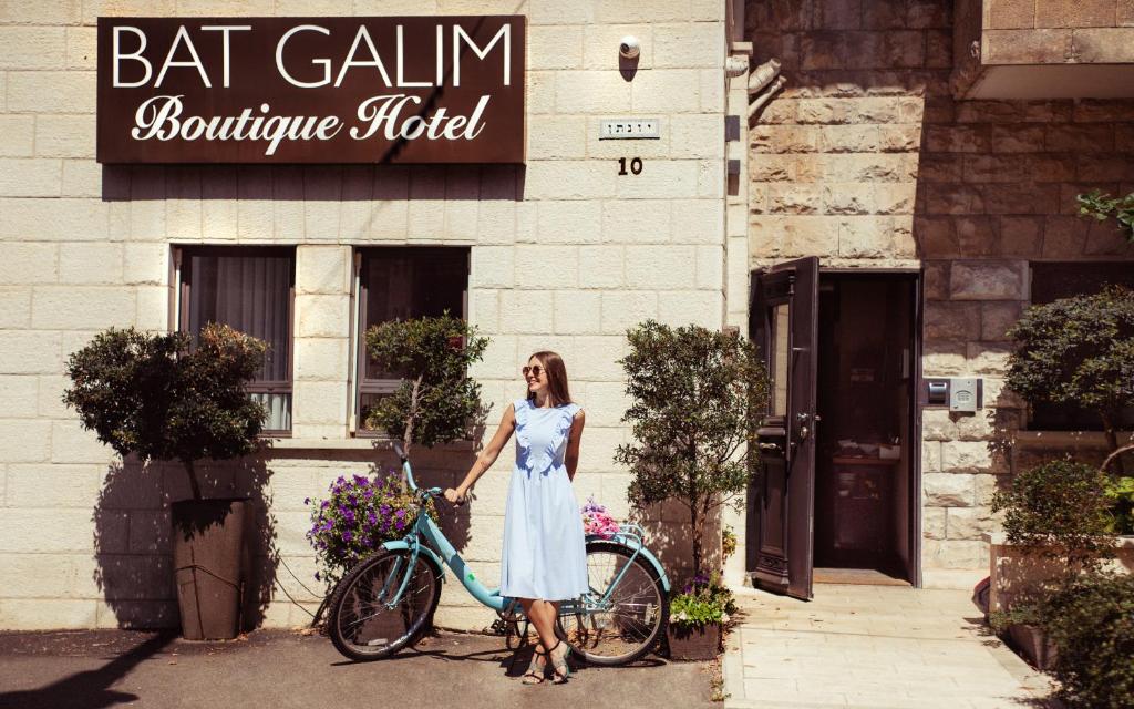 海法贝特咖里姆精品酒店的站在自行车旁的身着白色衣服的女人