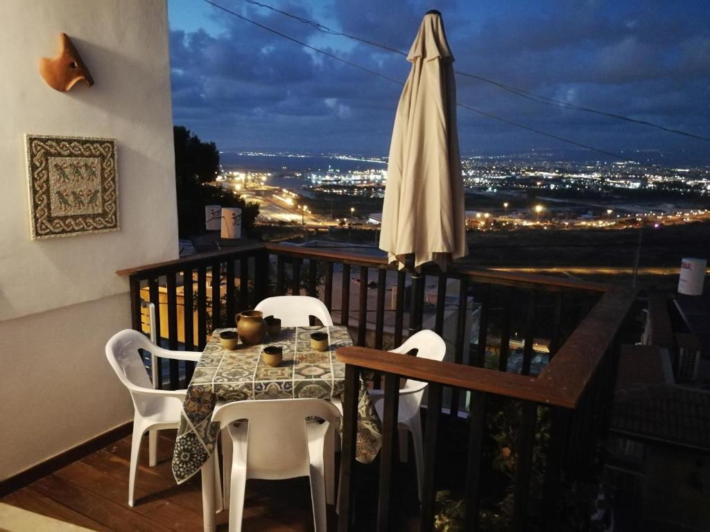 海法The Potter's House overlooking the Bay of Haifa的阳台配有桌椅和遮阳伞。