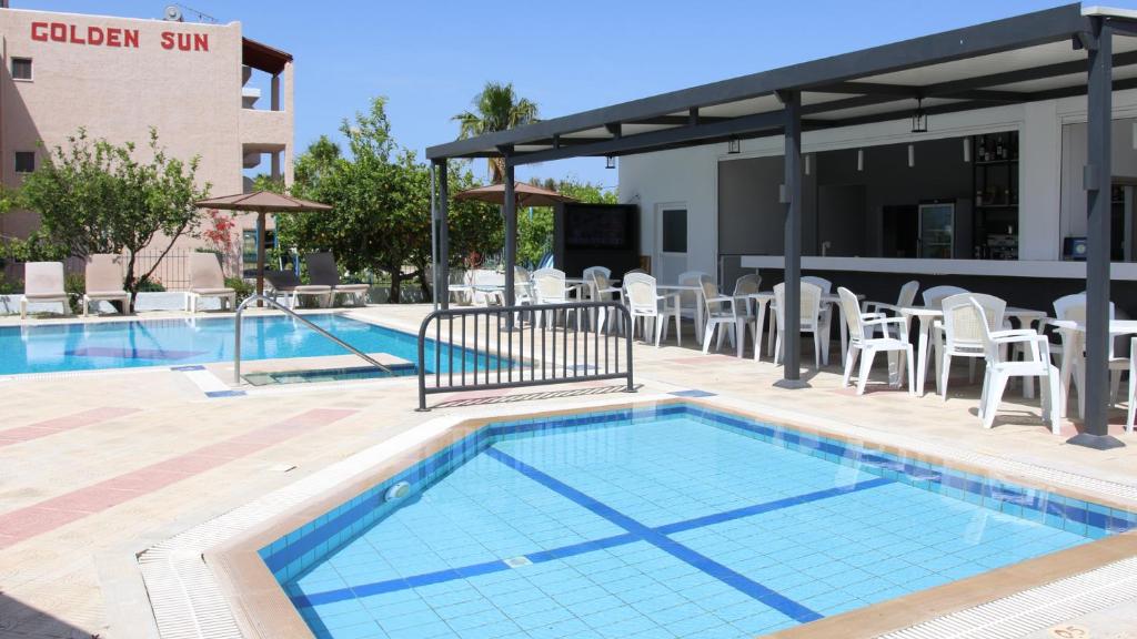 蒂加基金色阳光酒店的一座带白色椅子的游泳池和一座建筑