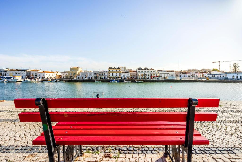 塔维拉马尔斯住宅酒店的坐在水体旁边的红色长凳