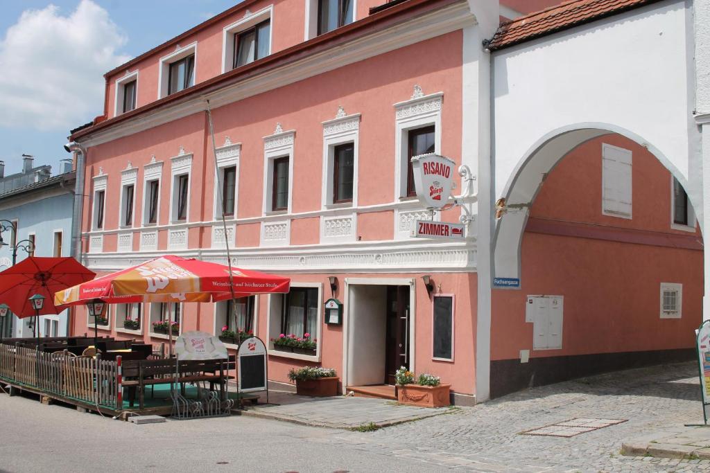 Haslach an der MühlGasthof-Cafe-Risano的粉红色的建筑,前面有桌子和雨伞