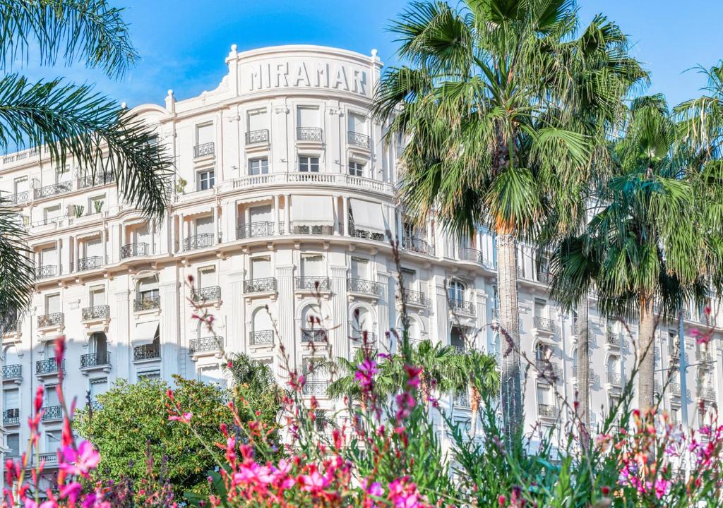 戛纳Palais Miramar Imperial Croisette的一座高大的白色建筑,前面有棕榈树