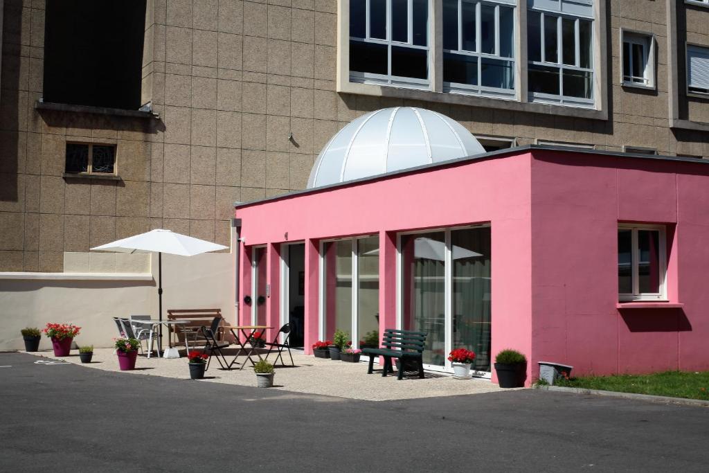 利雪Résidence La Providence ZENAO Lisieux的粉红色的建筑,配有桌子和雨伞