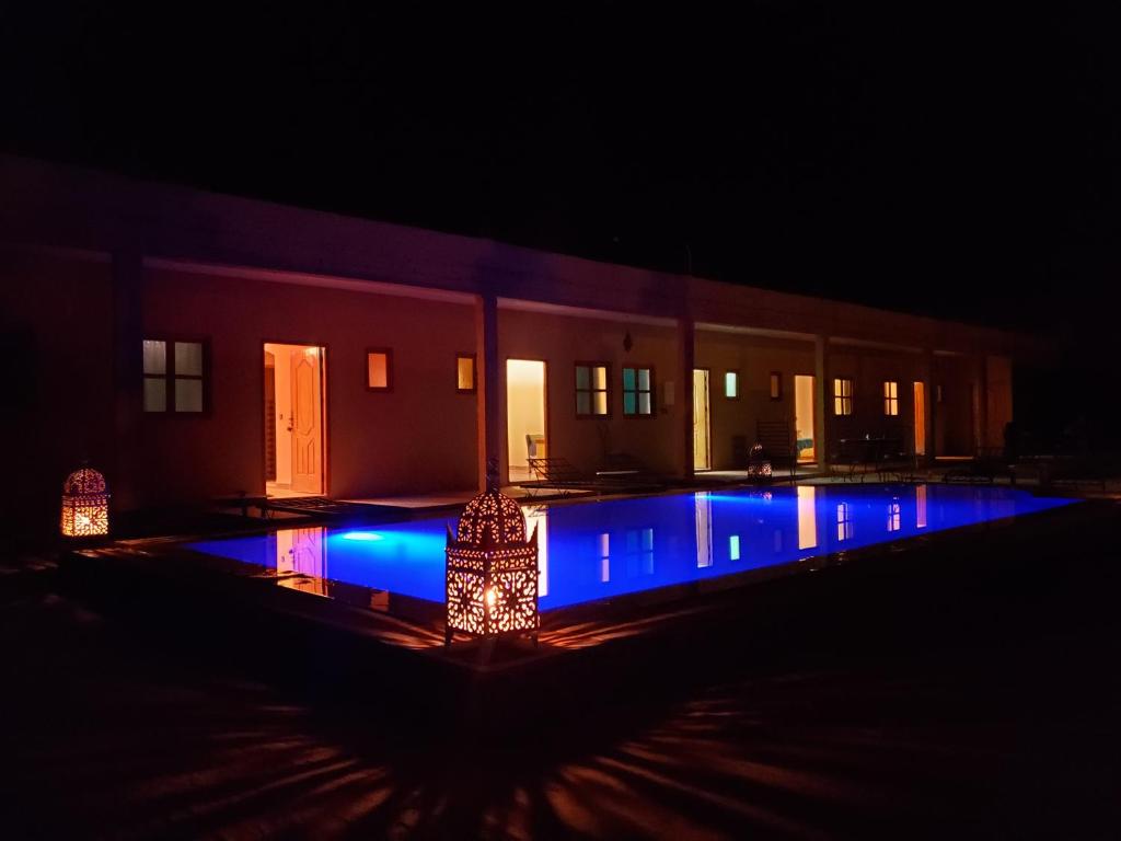 梅尔祖卡Riad Hotel Les Flamants的夜间在大楼前的蓝色灯光游泳池