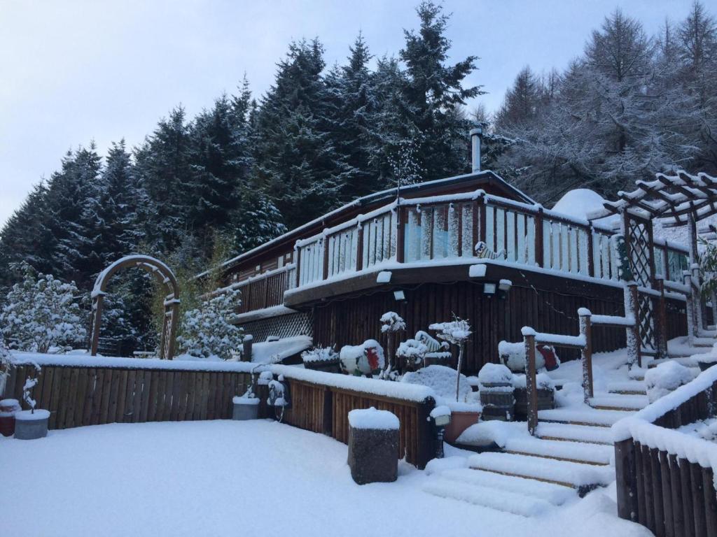 格伦德文Ramintoul Lodge的雪覆盖着楼梯和树木的房子