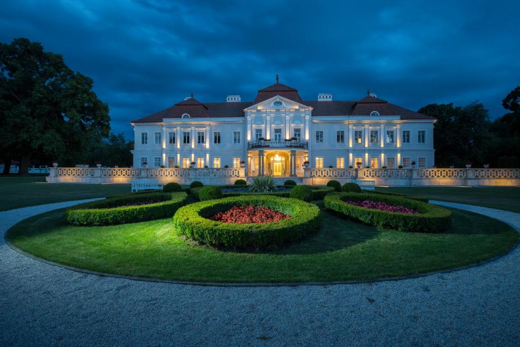 Tomášov艺术庄园酒店的一座白色的大宅邸,晚上设有花园