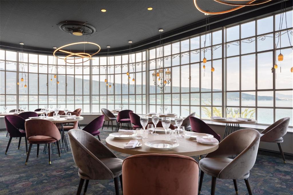 芒通圣贝尔纳门冬帕拉斯酒店的餐厅设有桌椅和大窗户。