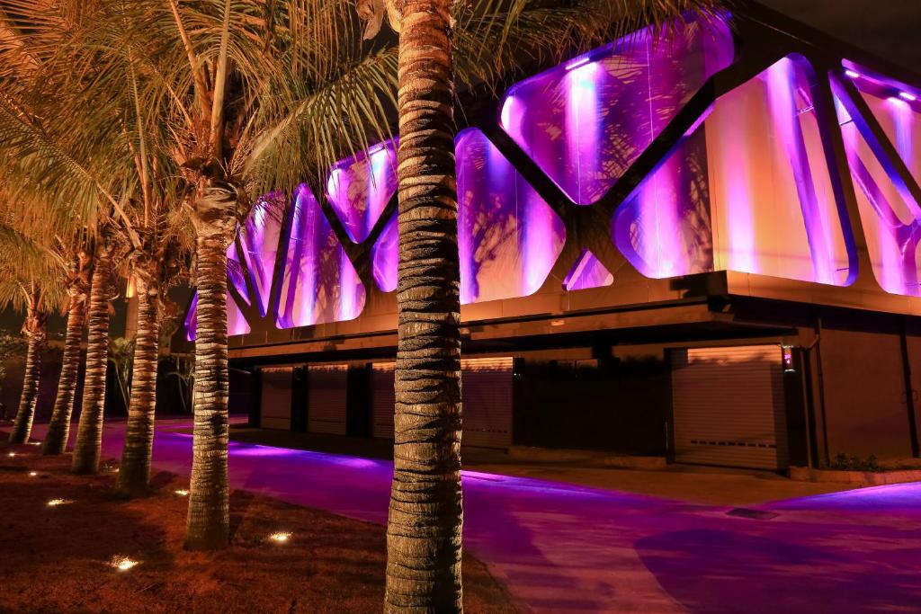 圣保罗Lush Motel Ipiranga的一座棕榈树的建筑,前面有紫色的灯光