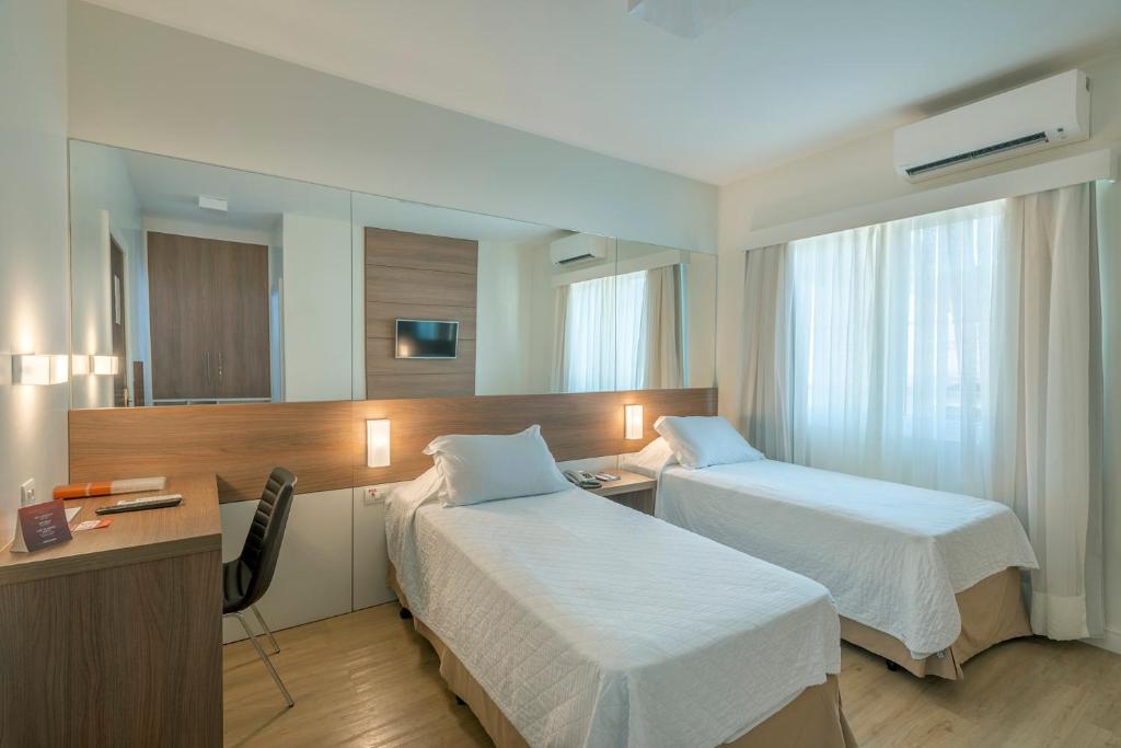 布卢梅瑙Hotel Glória Blumenau的酒店客房配有两张床和一张书桌