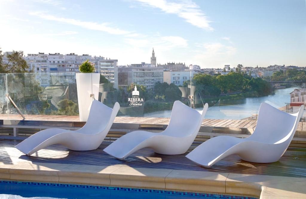 塞维利亚里贝拉特里亚纳酒店的游泳池边的三把白色椅子