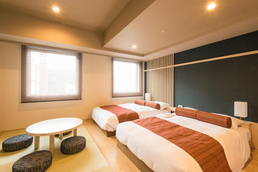 札幌Rembrandt Style Sapporo的一间卧室设有两张床、一张桌子和两个窗户。