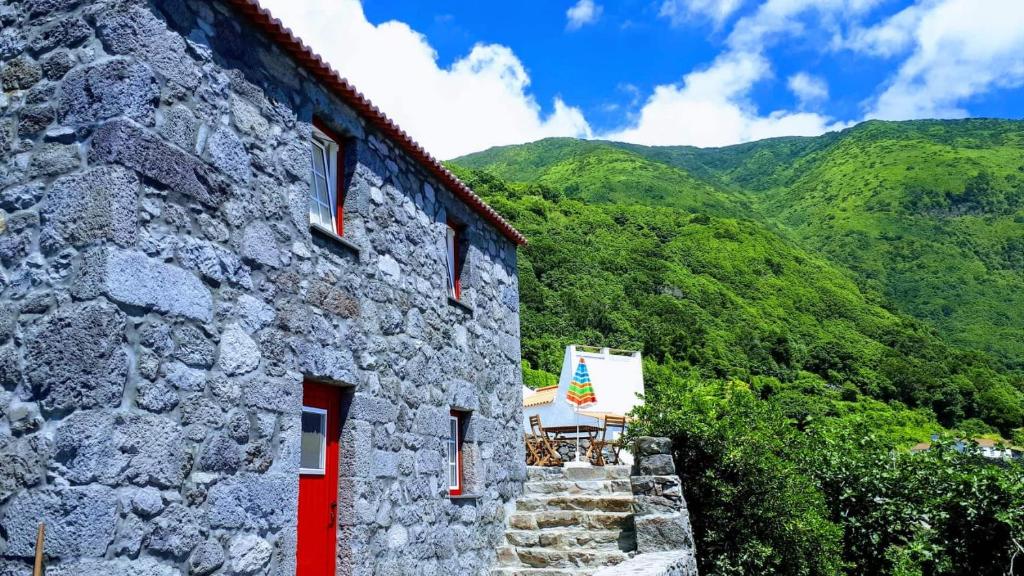 Fajã dos VimesCasa Grão de Café AL的一座石头建筑,设有红色的门,还有一些山脉