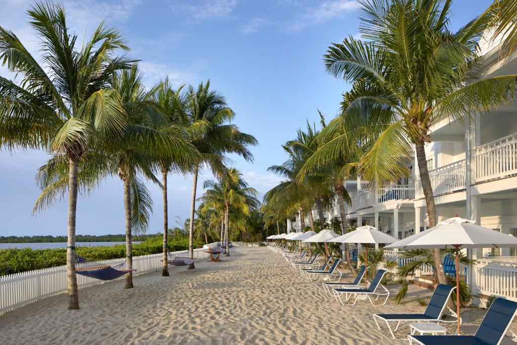 基韦斯特Parrot Key Hotel & Villas的海滩上,有椅子和棕榈树,还有一座建筑