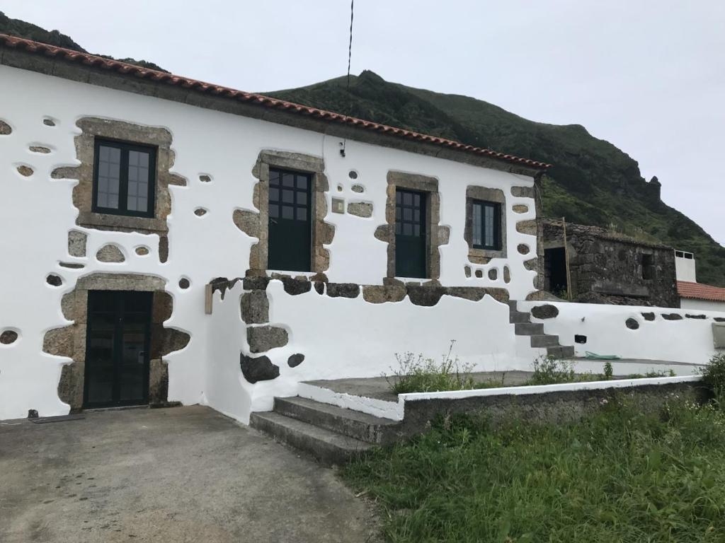 Lajes das FloresA casa do Tí Mendonça的一座白色的建筑,后面有一座小山