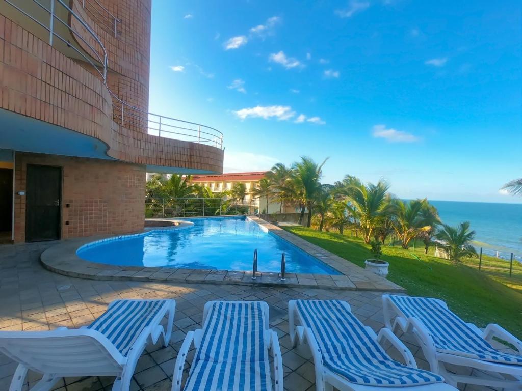 纳塔尔Costeira Praia Flat 204的一个带2把躺椅的游泳池和海洋