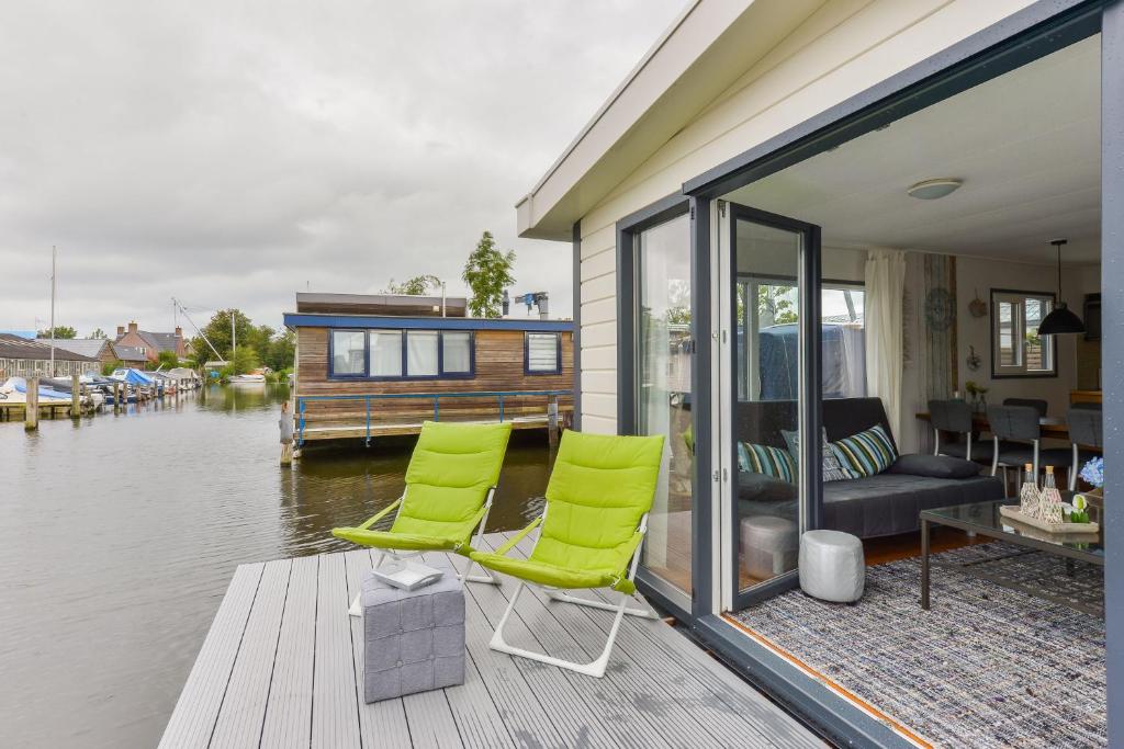 阿斯米尔Bright and Comfortable Houseboat的水边码头上两把绿色椅子的房子