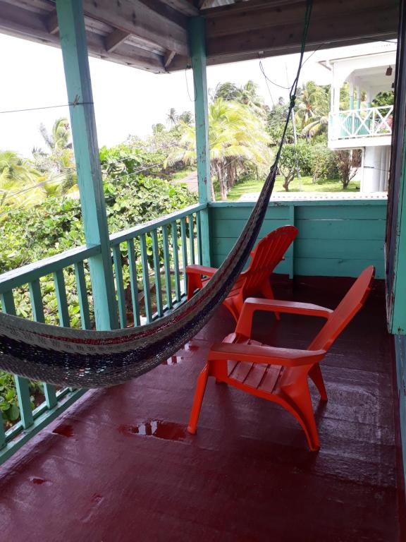 大玉米岛Corn Island Hostal ALAL SUITE的门廊上设有两张红色椅子和一张吊床