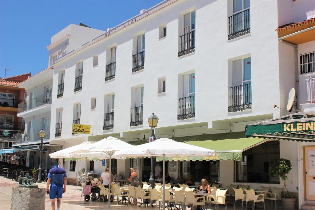 多列毛利诺斯Hotel Cabello的一座白色的大建筑,前面设有桌子和遮阳伞