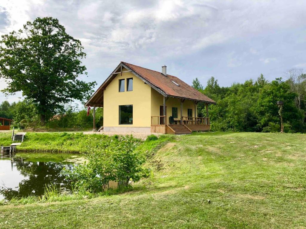 LīčiGuesthouse Sidrabozoli的一座小黄房子,位于一座带池塘的小山上