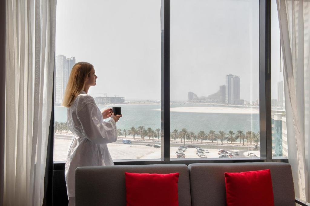 沙迦Novotel Sharjah Expo Centre的站在酒店房间,望向窗外的女人