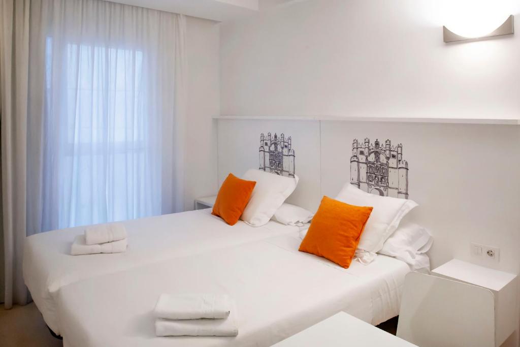 布尔戈斯玛丽亚莎乐美公寓式酒店的客房内的白色床,配有橙色和白色枕头