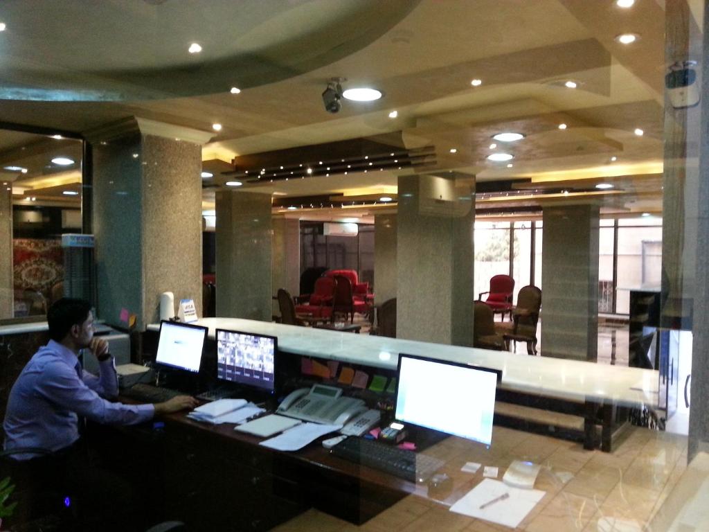 伊尔比德纳哈斯广场酒店的坐在一张桌子上,有三个电脑屏幕的人