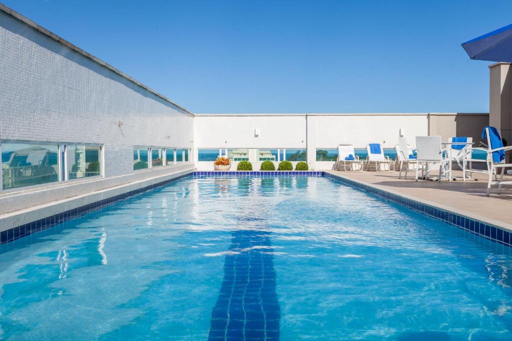 马卡埃Ramada by Wyndham Macae Hotel & Suites的大楼内带蓝色椅子的游泳池