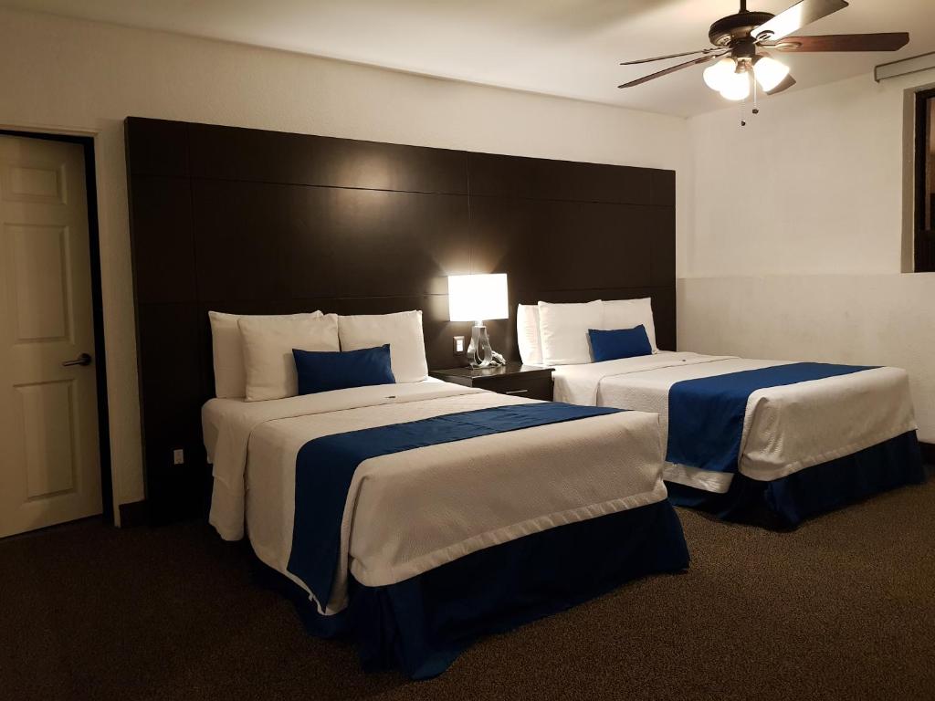 提华纳Hotel Principado Tijuana Aeropuerto的酒店客房带两张带蓝白床单的床。