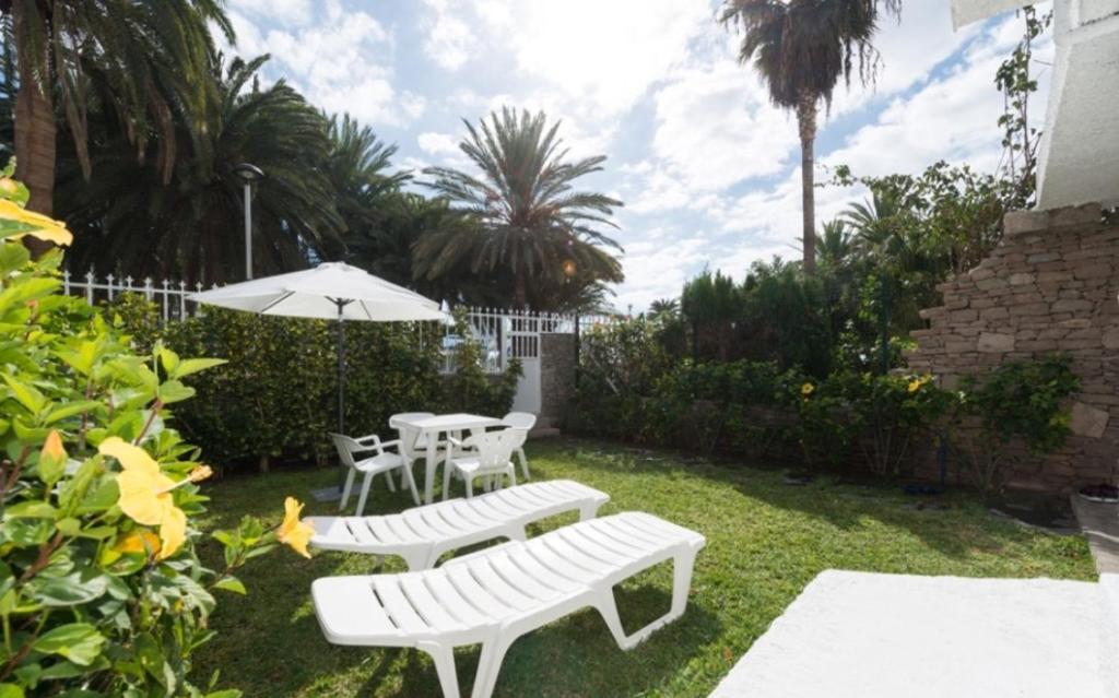 波多黎各Bonito Bungalow a pocos metros de la playa的庭院设有2个白色长椅和遮阳伞