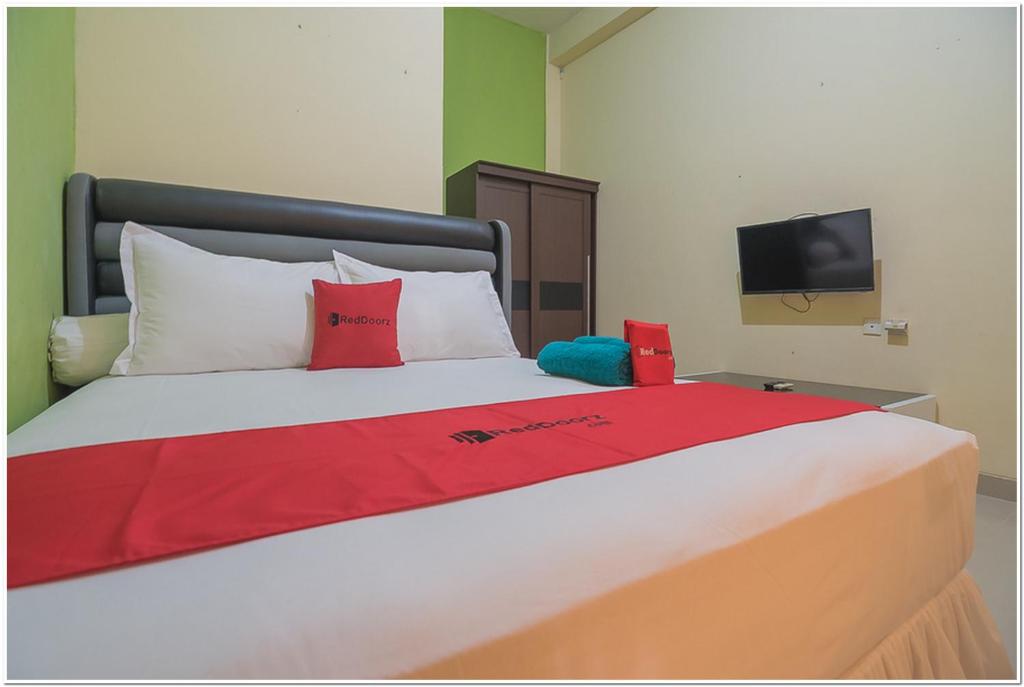 巴厘巴板RedDoorz near Lapangan Tenis Balikpapan的一张带红色和白色枕头的床以及电视