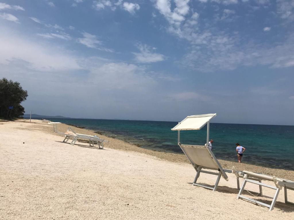 佩特坎内Nikola Luxury Apartments Senia的海滩上配有两把椅子和白色遮阳伞
