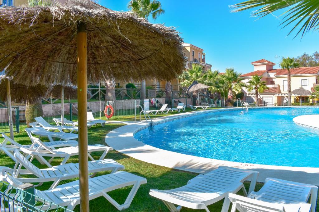 莱佩Disfrute de las playas y el golf en nuestro adosado en Islantilla - Costa de la Luz的一组椅子和一个带稻草伞的游泳池