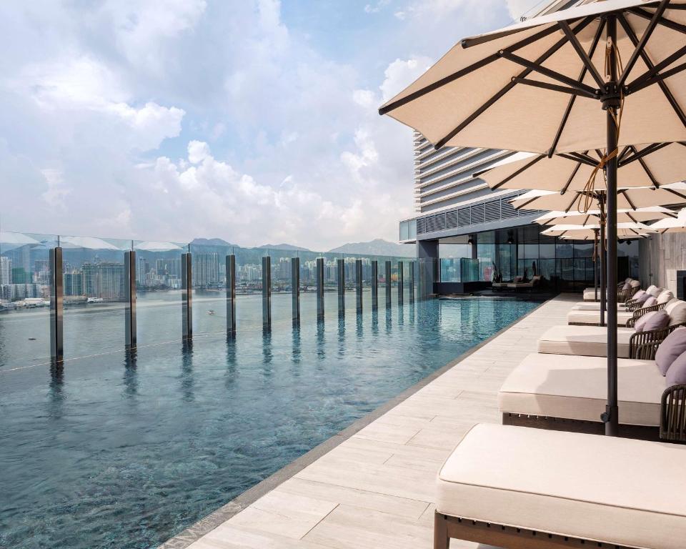 香港香港维港凯悦尚萃酒店的一座带椅子和遮阳伞的游泳池位于一座建筑旁边