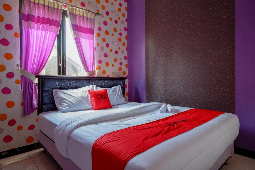 KebumenRedDoorz near RSUD Kebumen的一间卧室配有一张大床,铺有紫色和红色床单