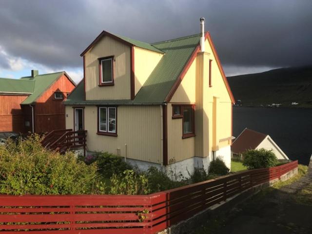 TrongisvágurDet lille gule hus的黄色的房子,有绿色的屋顶和红色的围栏
