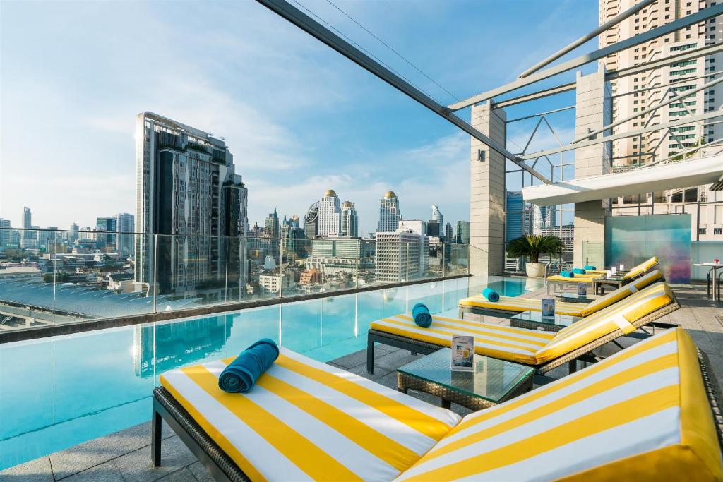 曼谷阿卡拉酒店的阳台设有黄色和白色的椅子和游泳池。