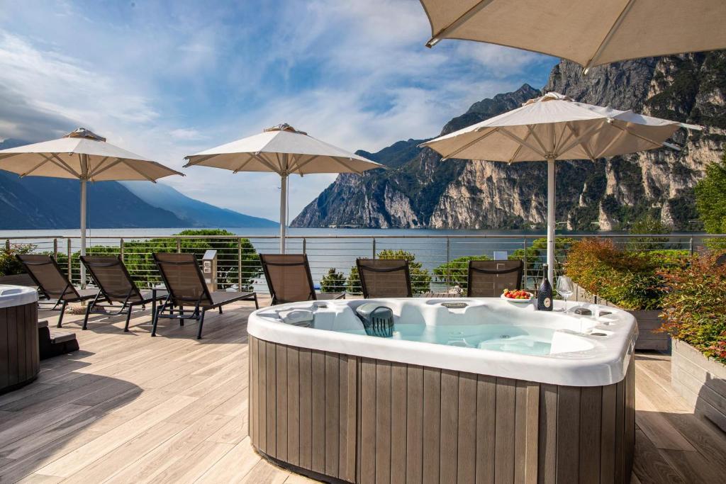 加尔达湖滨贝拉丽瓦酒店的甲板上的热水浴池配有椅子和遮阳伞