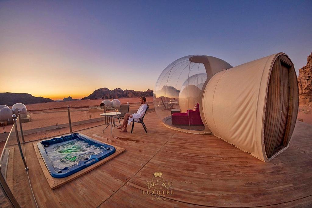 瓦迪拉姆Wadi Rum Bubble Luxotel的坐在帐篷和热水浴池旁椅子上的女人
