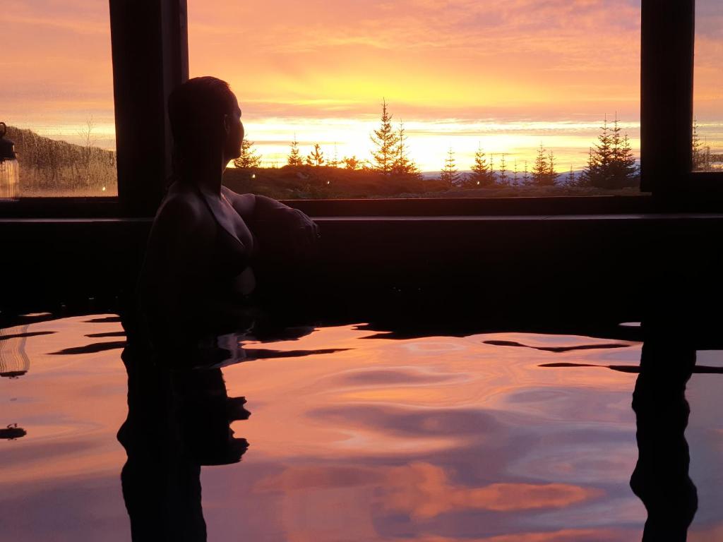 塞尔福斯360 Hotel & Thermal Baths的坐在浴缸中的女人,看着窗外的日落