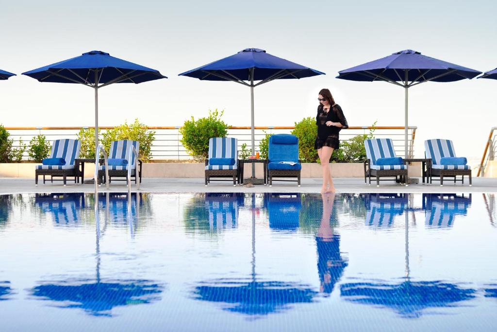 阿布扎比阿布扎比洲际酒店的一名妇女站在一个游泳池旁,游泳池边摆放着椅子和遮阳伞