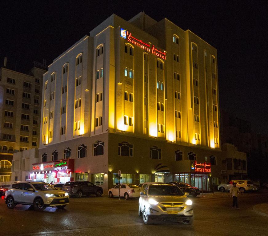马斯喀特萨马拉酒店的一座黄色的建筑,前面有汽车停放