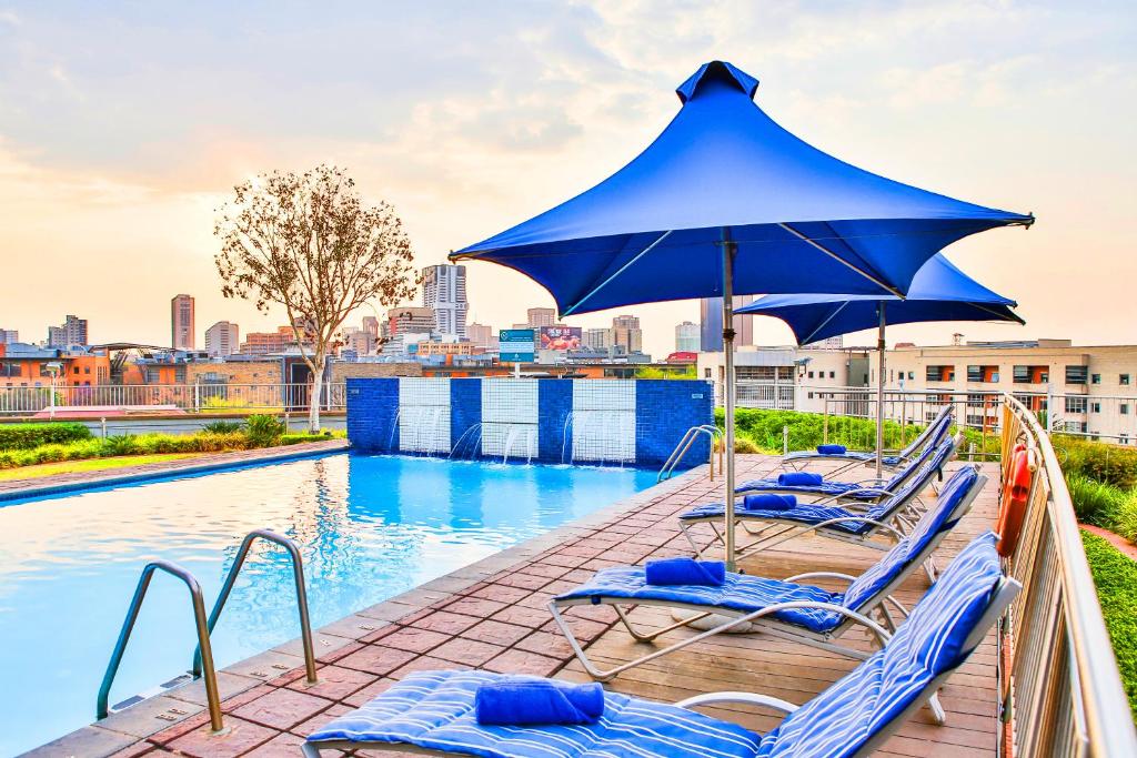 比勒陀利亚RH Hotel Pretoria的一组躺椅,在游泳池畔配有遮阳伞