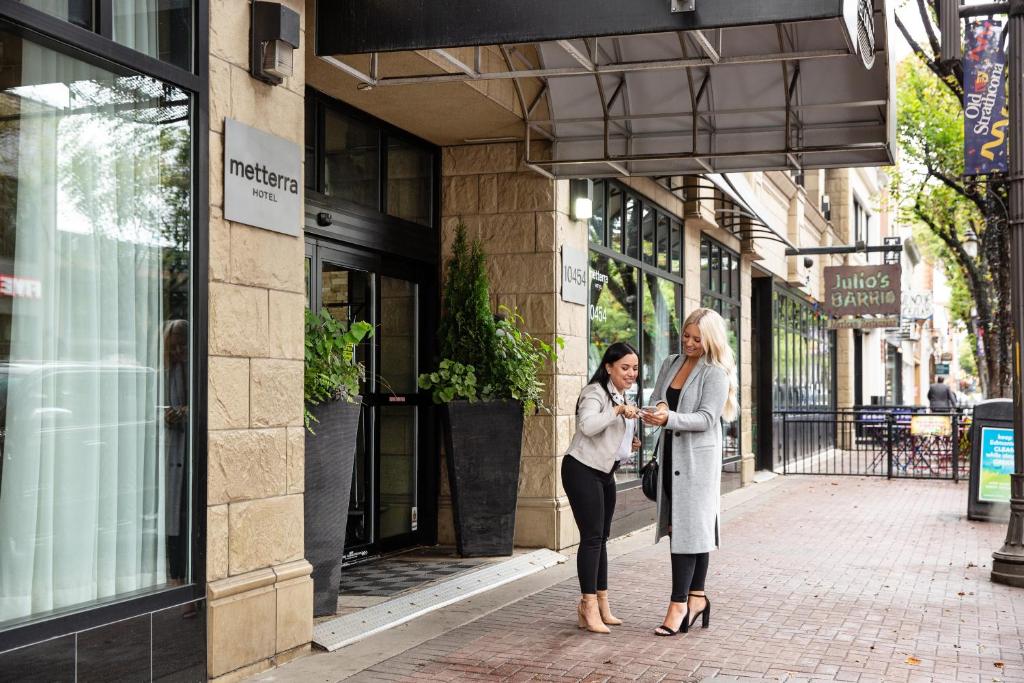 埃德蒙顿韦达米特拉酒店的两名妇女站在建筑物前面的人行道上