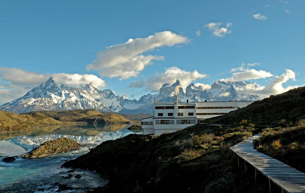 百内三塔Explora en Torres del Paine - All Inclusive的山丘上的一座建筑,毗邻一条有山脉的河流