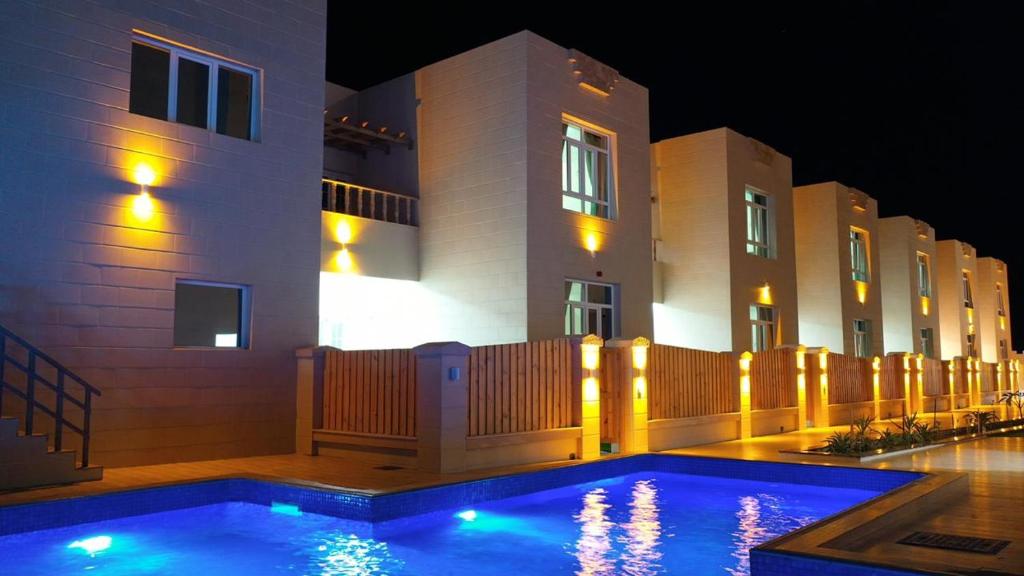 Al RuwisAl Asala Resort的一座游泳池,在晚上在建筑物前