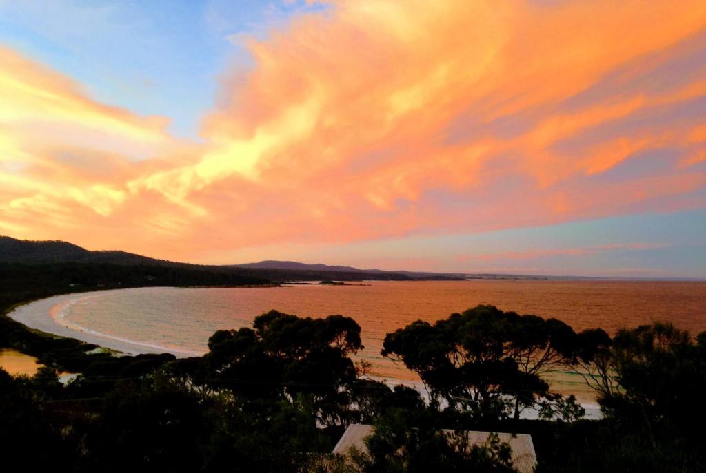 比那隆湾DOLPHIN LOOKOUT COTTAGE - amazing views of the Bay of Fires的海滩上方的日落美景,海滩上树木林立,