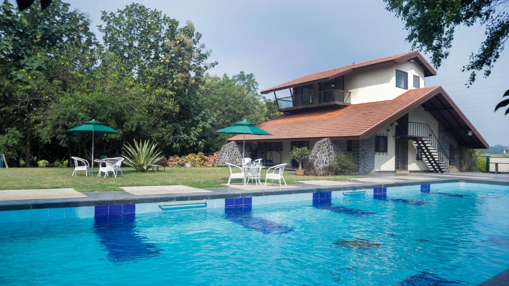 纳西克Jungle Safari Resort & Holiday Villa的一座房子,设有一座带椅子和遮阳伞的游泳池