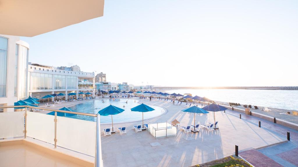 亚历山大Golden Jewel Hotel的一个带遮阳伞和椅子的游泳池以及大海