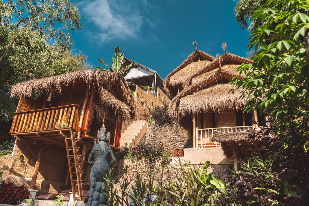 TampaksiringBALI BAMBOO JUNGLE HUTS AND HOSTEL的茅草屋顶的房子,前面有雕像